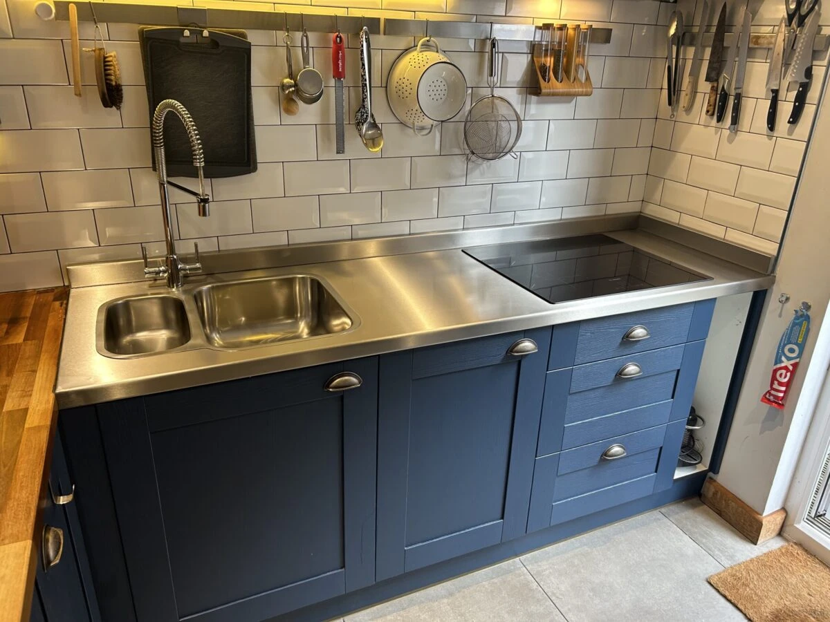 Shaker style blue kitchen cabinets, stainless steel worktop and integrated one and a half bowl sink plus modern mixer tap.